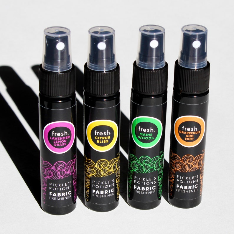 Puede incluir: Cuatro peque&ntilde;os frascos pulverizadores negros con etiquetas de diferentes colores. Las etiquetas tienen el texto "fresh." y una descripci&oacute;n del aroma. Los frascos est&aacute;n etiquetados con "Lavender Lemon Grass", "Citrus Bliss", "Maine Woods" y "Grapefruit and Mint". Los frascos est&aacute;n etiquetados con "Pickle's Potions Fabric Freshener".