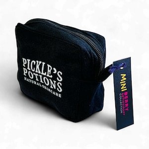 May include: A black canvas cosmetic bag with a zipper closure. The bag has the text "PICKLE'S POTIONS NATURAL SKINCARE" printed in white. A tag attached reads "MINI BERRY ANTIOXIDANT COLLECTION".