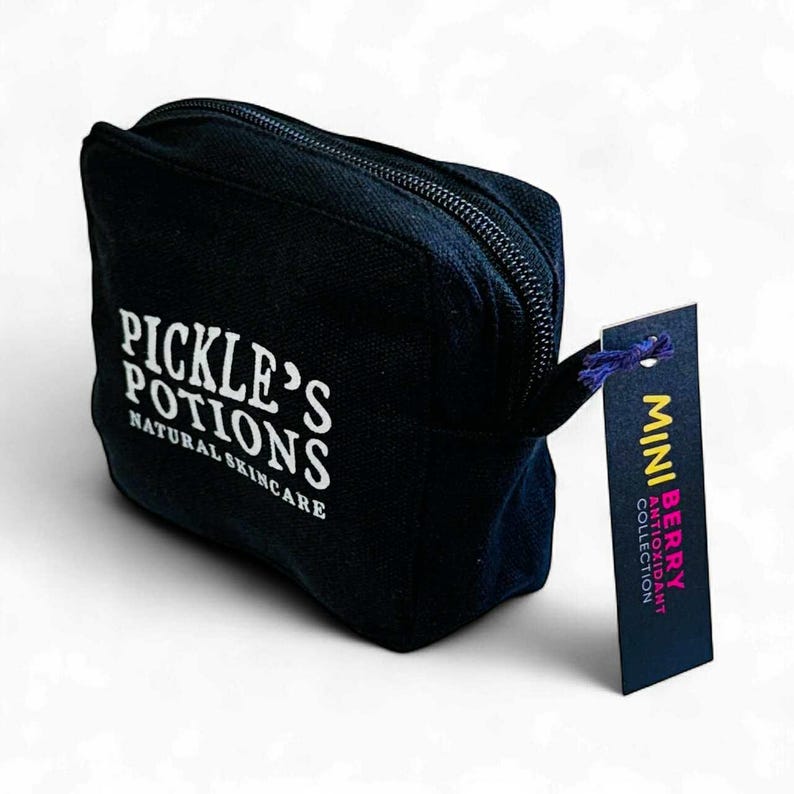 May include: A black canvas cosmetic bag with a zipper closure. The bag has the text "PICKLE'S POTIONS NATURAL SKINCARE" printed in white. A tag attached reads "MINI BERRY ANTIOXIDANT COLLECTION".