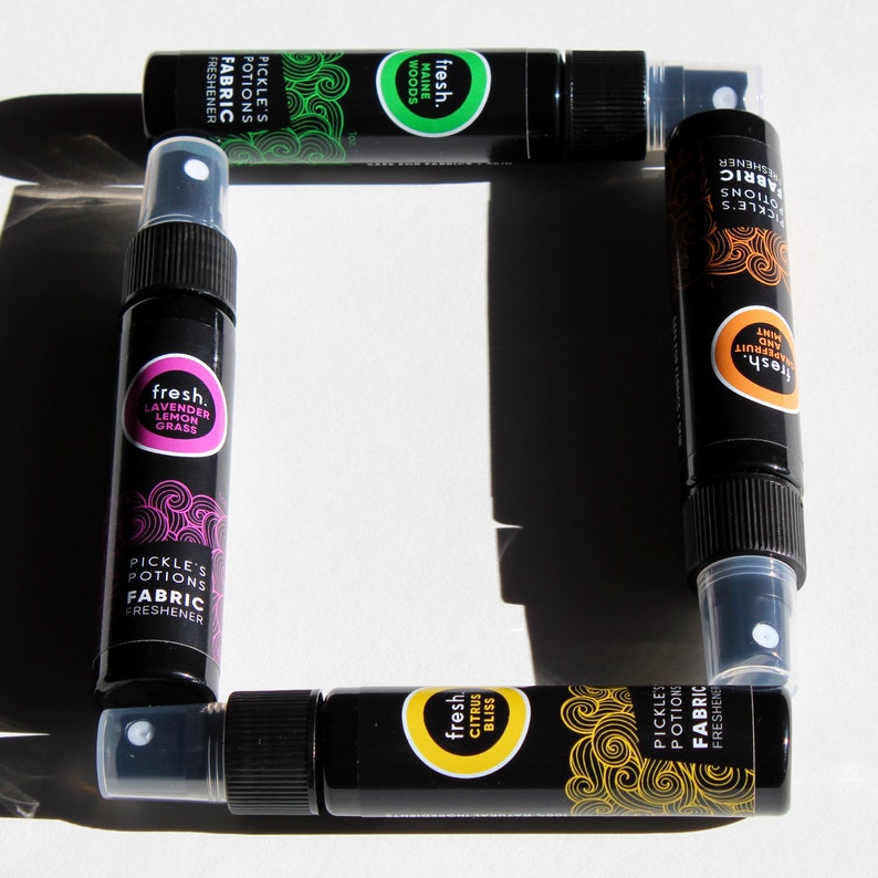 Puede incluir: Cuatro peque&ntilde;os frascos pulverizadores negros con etiquetas de colores. Las etiquetas muestran el texto "fresh." y "Pickle's Potions Fabric Freshener" junto con diferentes aromas como "Lavender Lemon Grass", "Maine Woods", "Citrus Bliss" y "Mint and Grapefruit".
