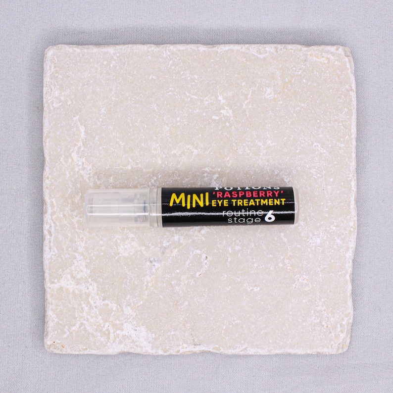 Op de afbeelding: Een klein zwart-wit flesje met de tekst "MINI 'RASPBERRY' EYE TREATMENT routine stage 6" erop.