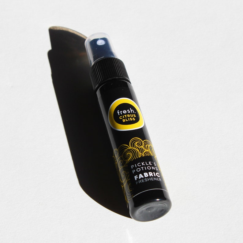 Puede incluir: Una botella de spray negra con una etiqueta amarilla que dice "fresh. citrus bliss pickle's potions fabric freshener".