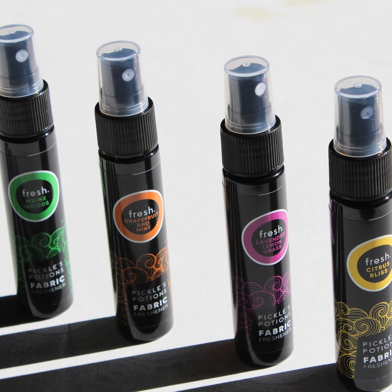 Puede incluir: Cuatro peque&ntilde;os frascos pulverizadores negros con etiquetas de diferentes colores. Las etiquetas tienen el texto "fresh." y una descripci&oacute;n del aroma. Los frascos est&aacute;n etiquetados como "Pickle's Potions Fabric Freshener".