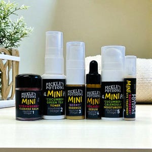 May include: A collection of six mini skincare products from Pickle's Potions. The set includes a strawberry cleanse balm, cucumber green tea toner, berry essence, rosacea serum, cucumber calendula moisturizer, and raspberry eye treatment. Each product is labeled with its name and routine stage.