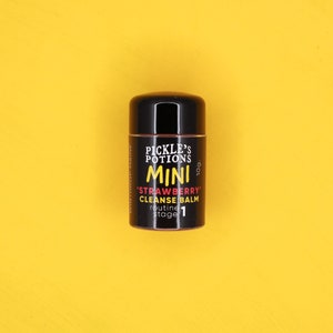 May include: A small, black and white container of 'Pickle's Potions' 'Strawberry' Cleanse Balm, labeled 'Mini' and 'routine stage 1'.