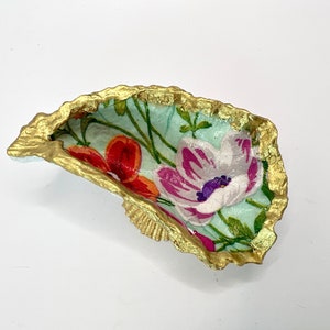 May include: A small, decorative oyster shell dish with a gold rim. The inside of the shell is painted with a floral pattern in shades of pink, red, white, and green.