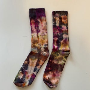May include: A pair of colorful socks with a tie-dye pattern in shades of purple, orange, and black. The socks are labeled "Black Opal".
