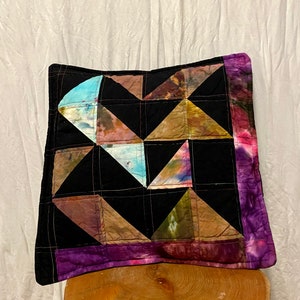 May include: A black and purple patchwork pillow with a geometric design. The pillow is made of different fabrics with a tie-dye effect.