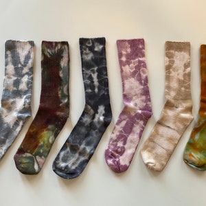 May include: Six pairs of colorful tie-dye socks. The socks are all different colors and patterns, including blue, purple, brown, and orange.