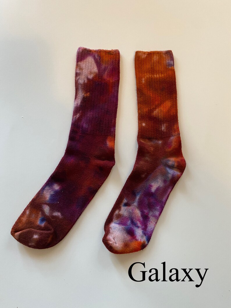 May include: A pair of tie-dye socks in shades of purple, orange, and brown. The socks have a galaxy-like pattern and are labeled "Galaxy".