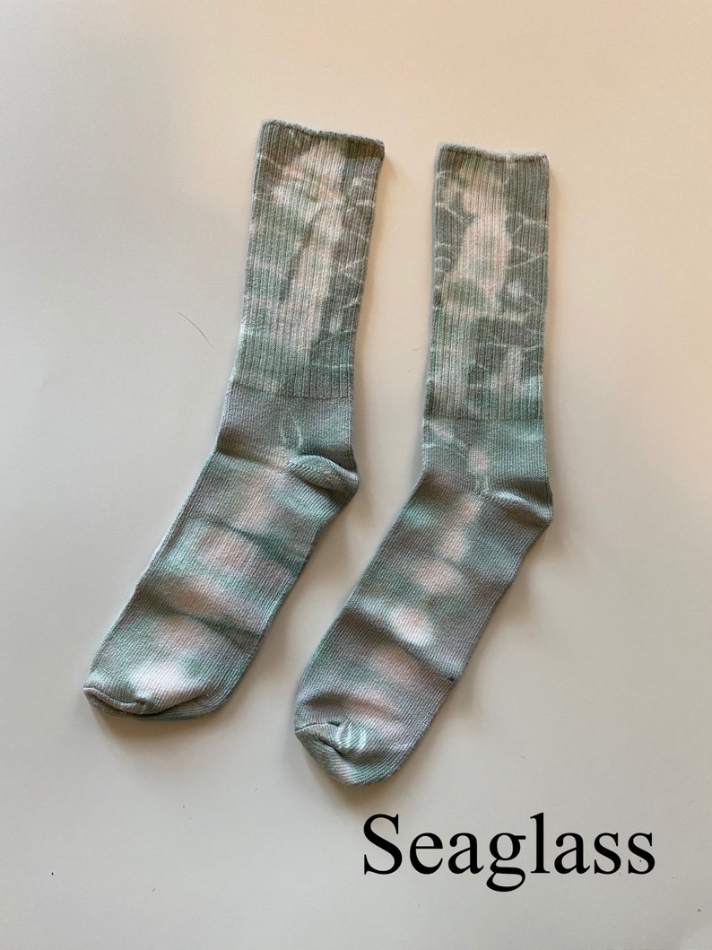 May include: A pair of green and white tie-dye socks with the word "Seaglass" written below them.
