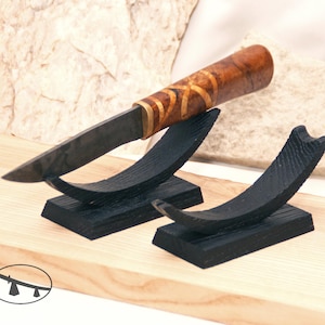 May include: A handcrafted knife with a wooden handle featuring a decorative pattern and a dark blade, displayed on a black wooden stand. The knife is resting on a wooden surface, showcasing its craftsmanship and design.