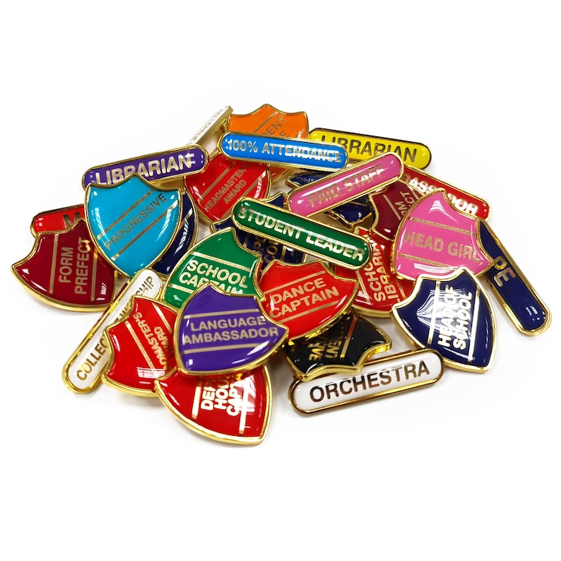 May include: A collection of colorful enamel pins with gold trim. The pins feature various school-related titles, such as "Head Girl", "School Captain", "Dance Captain", "Librarian", "Form Prefect", "Student Leader", "Language Ambassador", "Head of School", "100% Attendance", "Orchestra", and "College Masters".