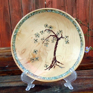 Peut inclure: Un bol en bois avec un motif d'arbre incrusté de pierres vertes et blanches irisées. Le bol est sur un support en plastique transparent.