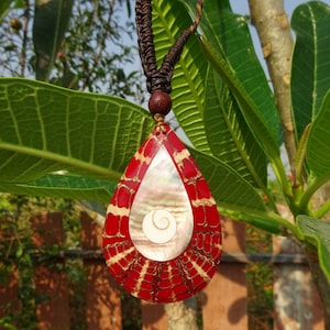 May include: A teardrop-shaped pendant necklace with a red and gold patterned design. The pendant features a white mother-of-pearl inlay with a spiral pattern.