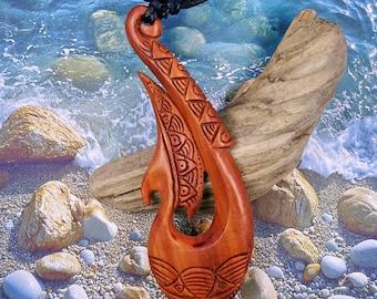 May include: A carved wooden pendant in a fish hook design, featuring intricate patterns and a natural wood finish. The pendant hangs from a black cord, showcasing a Polynesian-inspired aesthetic. The pendant is approximately 4 inches long.