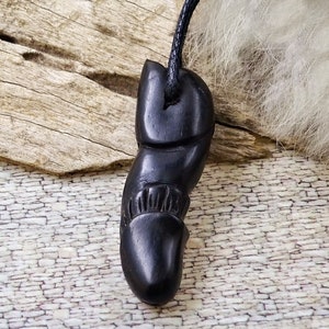 Könnte beinhalten: Ein schwarzer, geschnitzter Anhänger mit einem detaillierten Design, der an einer schwarzen Schnur hängt.