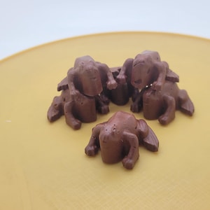 May include: Four small chocolate frogs on a yellow plate. The frogs are brown and have detailed features.