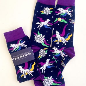May include: A pair of dark blue socks with a purple cuff. The socks feature a colourful pattern of white wolves howling at the moon, white flowers, and stars. The socks have the text "Northern Lights Wolves Patterned Socks" on a black tag.