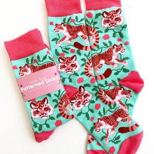 May include: A pair of teal and pink socks with a leafy tiger pattern. The socks have a pink cuff and a tag that reads "Leafy Tiger Patterned Socks".