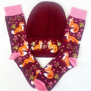 Pode incluir: Um conjunto de duas meias de raposa bord&ocirc; com acabamento rosa e um gorro de tric&ocirc; bord&ocirc; com um design de raposa.