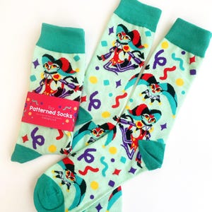 Puede incluir: Un par de calcetines verdes con un patrón colorido que presenta un bufón de dibujos animados. Los calcetines están sobre un fondo blanco. El texto en la etiqueta dice "Fizz Patterned Socks".