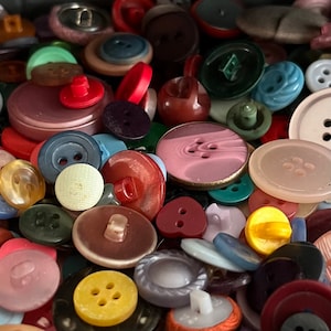 May include: A collection of colourful buttons in various shapes and sizes, including round, square, and heart-shaped buttons. The buttons are made of different materials, such as plastic, metal, and wood. Some buttons have intricate designs, while others are plain.