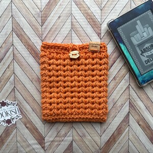 May include: Orange crochet e-reader cover with a wooden button and a small brown tag that says "Crocheting Ginger".