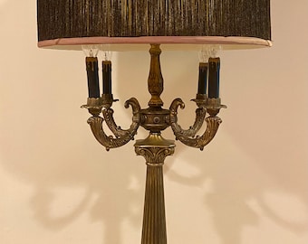 May include: A gold-toned table lamp with a five-arm candelabra design. The lamp has a black fringed lampshade with a pink lining.