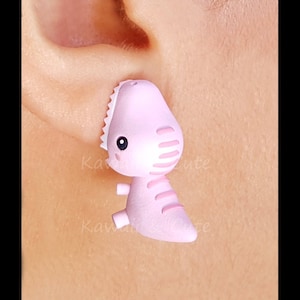 May include: Pink dinosaur shaped earrings. The dinosaur has a cute face and is made of polymer clay.
