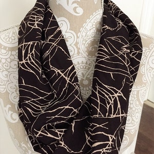 May include: A brown infinity scarf with a beige abstract pattern of branches.