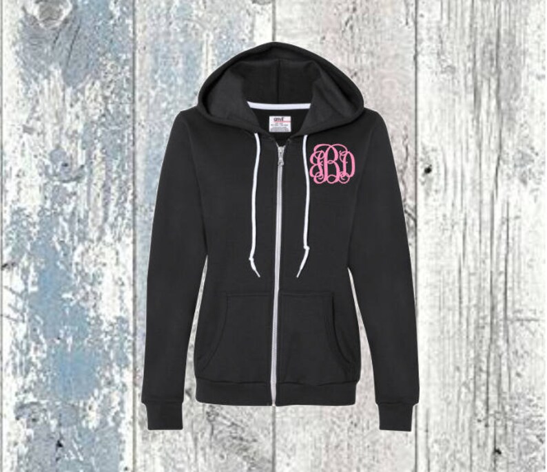May include: A black zip-up hoodie with a white zip and white drawstrings. The hoodie has a pink monogram on the front that says "BD".