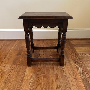 May include: A dark brown wooden side table with a rectangular top, featuring four turned legs connected by a lower rectangular stretcher base. The apron beneath the tabletop has a scalloped edge design, showcasing a natural wood grain finish.