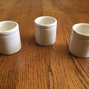 May include: Three white ceramic jars with a simple design. The jars are all the same size and shape, and they have a smooth, white finish.