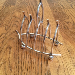 May include: Silver plated toast rack with five prongs and a curved base. The rack is made of metal and has a shiny finish.