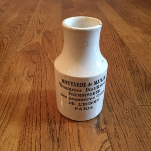 May include: White ceramic mustard jar with a blue and white label that reads "MOUTARDE de MAILLE Vinaigrier Distillateur FOURNISSEUR des premieres Cours DE L'EUROPE PARIS".
