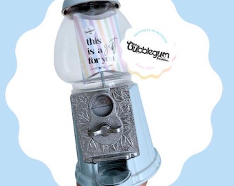 May include: A light blue gumball machine with a silver coin slot and a clear glass jar. The machine has a sign that says "This is a gift for you".