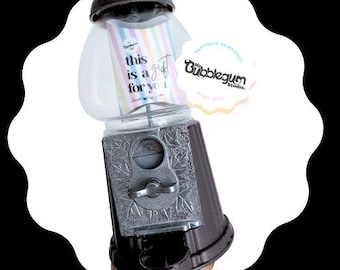 May include: A vintage-style gumball machine with a clear plastic container and a silver metal base. The machine has a sign that says "This is a gift for you".