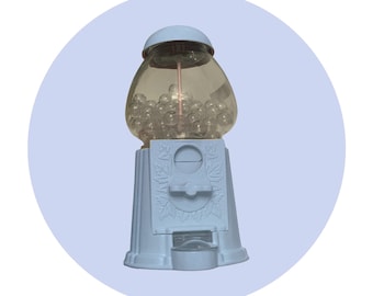 May include: A white plastic gumball machine with a clear plastic container filled with white gumballs. The machine has a white base with a decorative design.