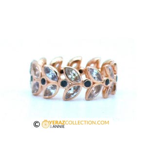 Puede incluir: Un anillo de oro rosa con un delicado dise&ntilde;o de hojas y piedras preciosas transparentes. El anillo est&aacute; engastado con piedras preciosas negras entre cada hoja.