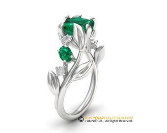Könnte beinhalten: Ein silberner Ring mit einem grünen Smaragd-Edelstein und kleineren grünen Smaragden und Diamanten, die in einem floralen Design gesetzt sind.