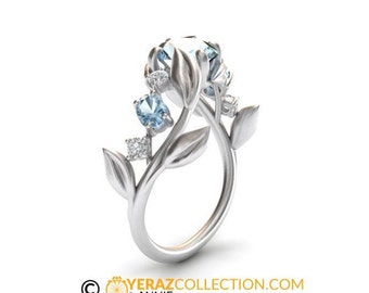 May include: A silver ring with a delicate floral design featuring blue gemstones and smaller clear stones. The ring is set on a white background.