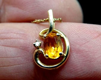 Op de afbeelding: Gouden hanger met een ovale gele edelsteen en een kleine diamant. De hanger hangt aan een fijne gouden ketting. Het ontwerp heeft een wervelende, open gouden zetting.