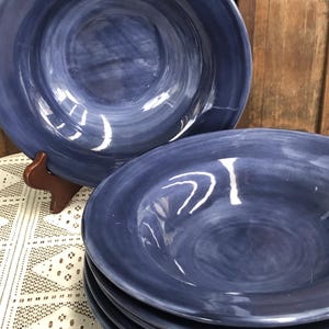 May include: A stack of six deep blue ceramic bowls with a marbled effect. The bowls have a wide rim and a rounded shape. The bowls are stacked on a white lace tablecloth.