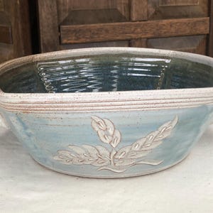 May include: A handmade ceramic serving bowl with a light blue exterior and a dark blue interior. The bowl features a raised leaf design and two small handles. The rim is white and the bowl is approximately 12 inches long.