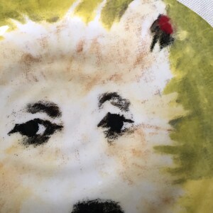 May include: A ceramic plate with a dog's face design. The dog has black eyes, a white face, and a light brown nose. The background is a mix of yellow and green.
