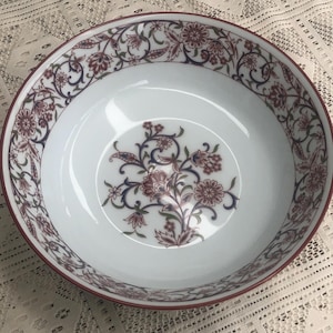 May include: White ceramic serving bowl with a floral design in burgundy, blue, and green. The rim and the central floral motif are burgundy. The bowl has a wide, shallow shape, suitable for serving salads or pasta.