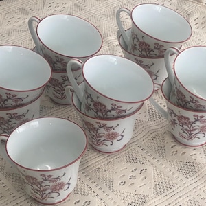 May include: A set of eight white teacups with a floral pattern in shades of pink and red. The cups have a delicate design and are perfect for a tea party or afternoon tea.