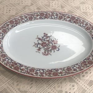 May include: An oval serving platter with a white background and a red and blue floral design around the edge.