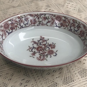 May include: White oval serving bowl with a red and blue floral pattern around the rim. The bowl has a single floral design in the center.